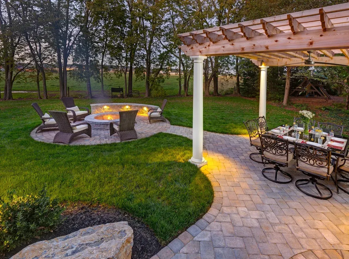 A patio with a fire pit and a table and chairs under a pergola.