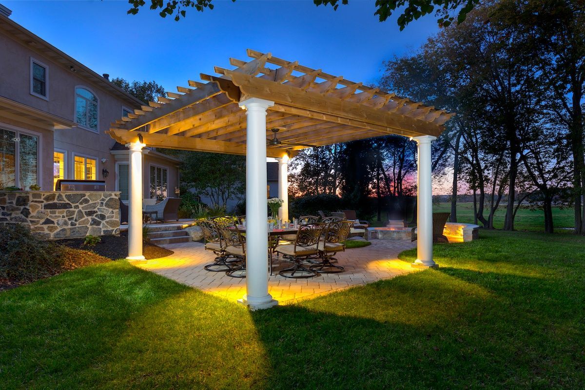 A pergola with a table and chairs underneath it in a backyard at night.