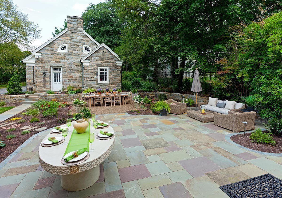 A patio with a table and chairs in front of a stone house.