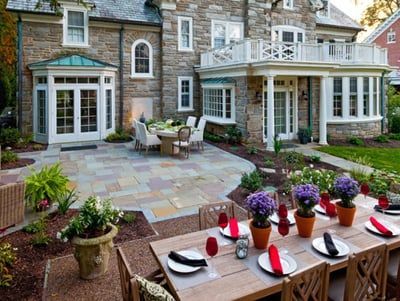 A patio with a table and chairs in front of a large stone house.