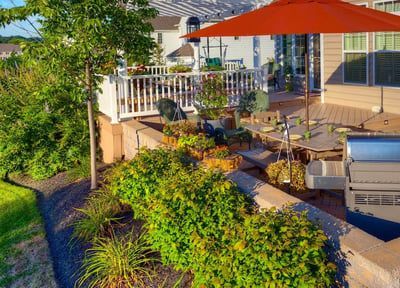 A red umbrella is sitting on a patio next to a grill.