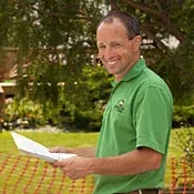 A man in a green shirt is holding a piece of paper and smiling.