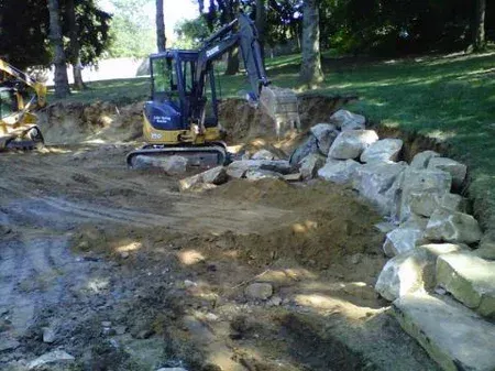 A small excavator is digging a hole in the ground next to a pile of rocks.