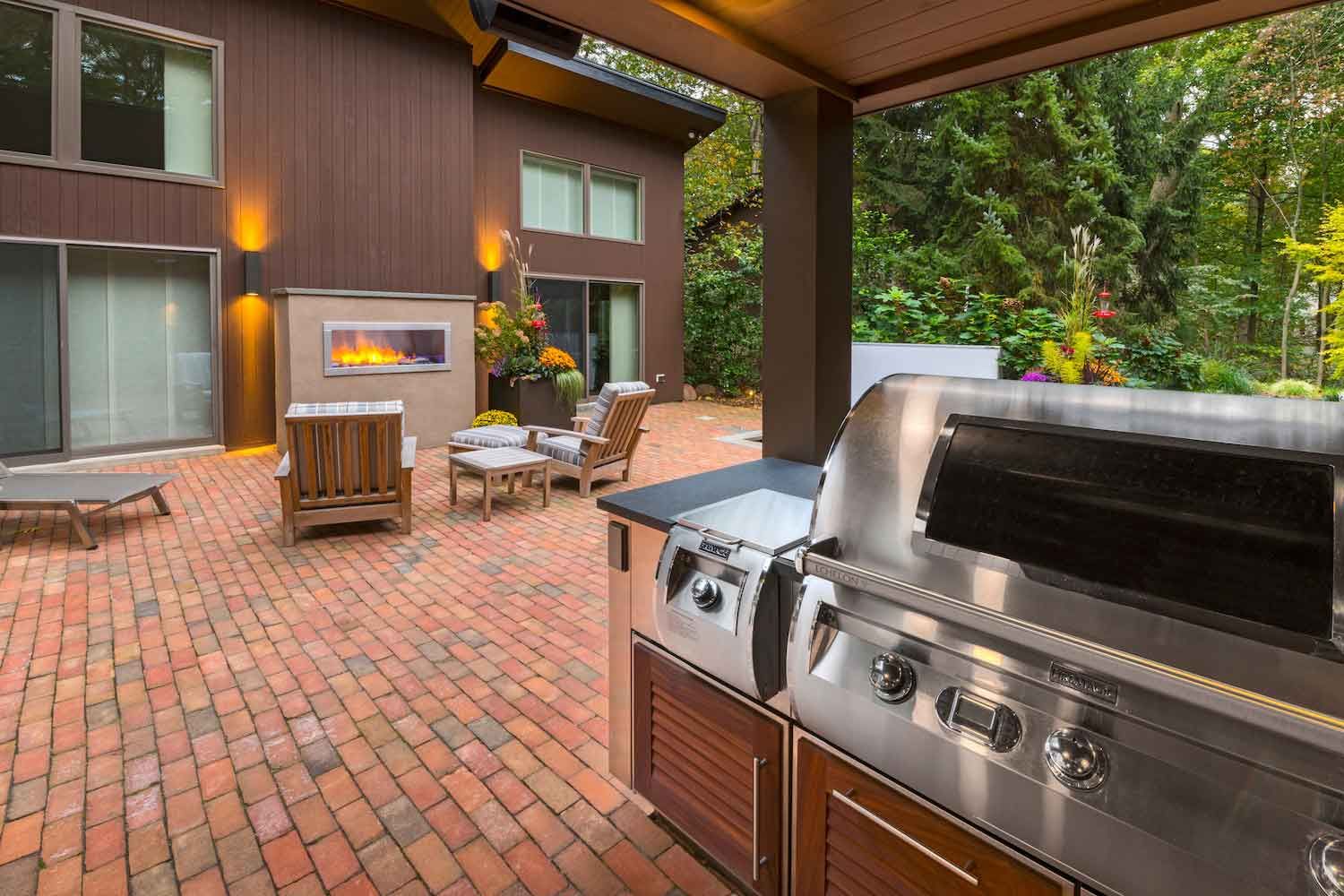 A patio with a grill and a fireplace in front of a house.