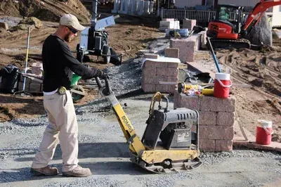 A man is using a vibratory plate compactor on a construction site.