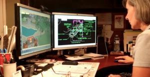 A woman is sitting at a desk in front of two computer monitors.