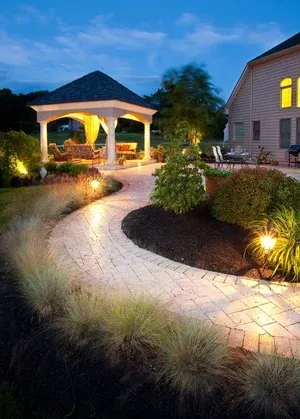 A gazebo is lit up at night in the backyard of a house.
