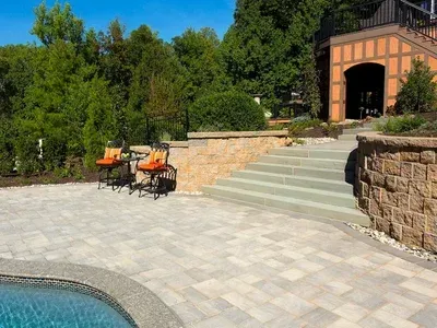 A patio with chairs and tables next to a pool and stairs leading to a garage.