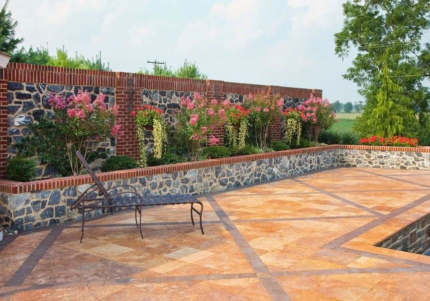 A brick wall surrounds a patio with a bench and flowers