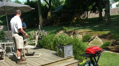 A man is standing on a deck next to a grill.