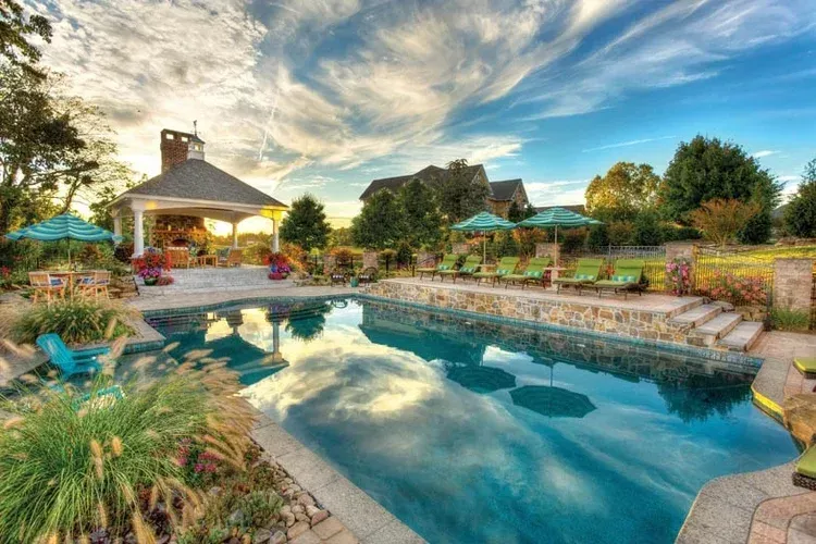 A large swimming pool surrounded by chairs and umbrellas with a gazebo in the background.