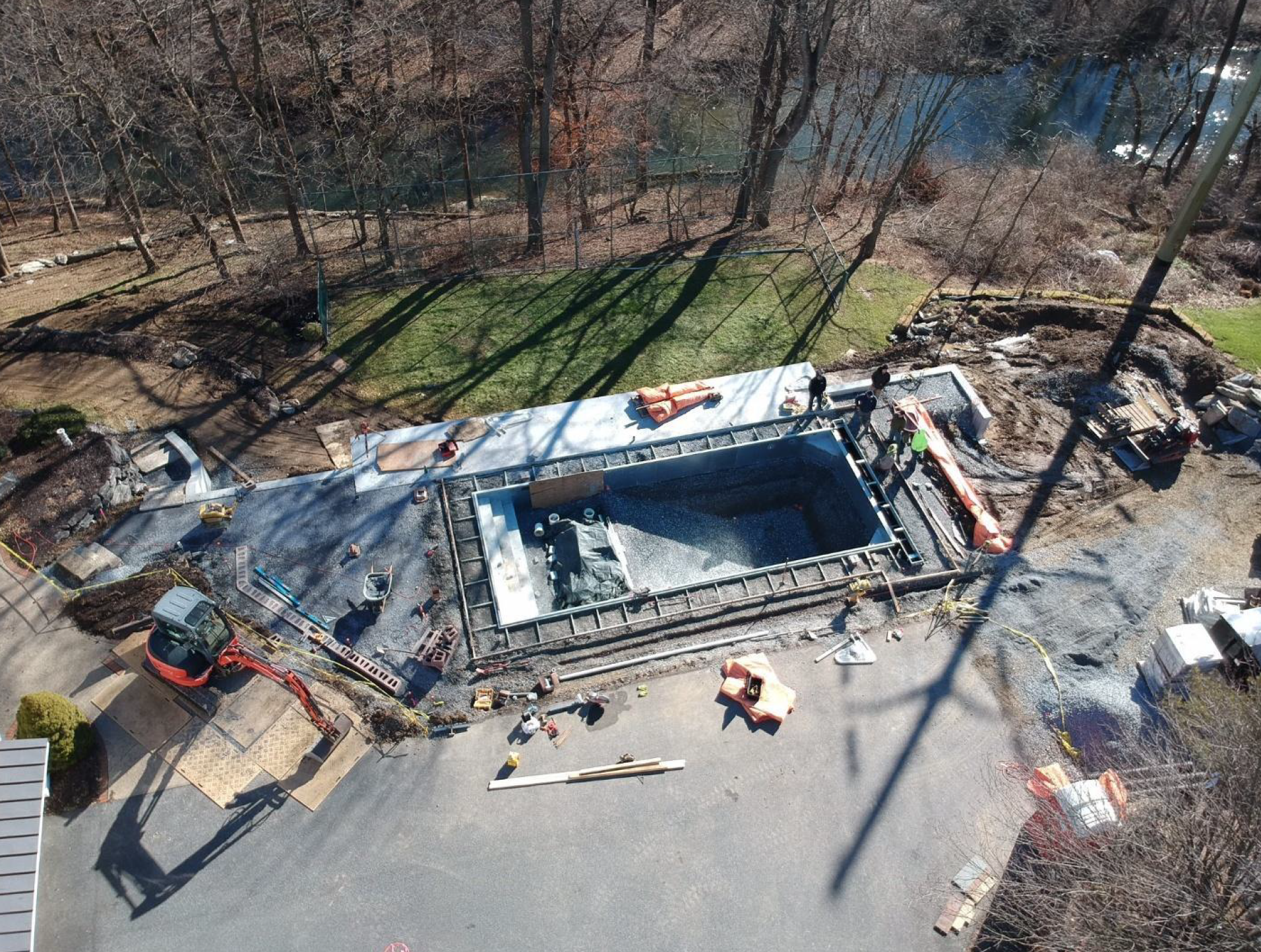 Aerial view of an in-ground pool construction site with workers, machinery, and scattered materials.