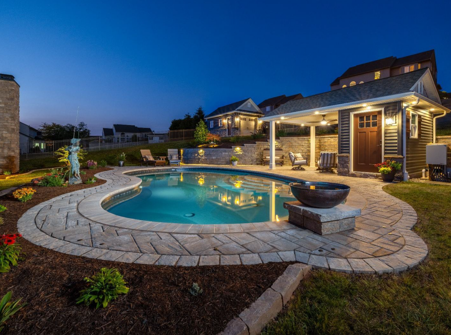 Illuminated backyard pool with stone patio and a lit gazebo at dusk