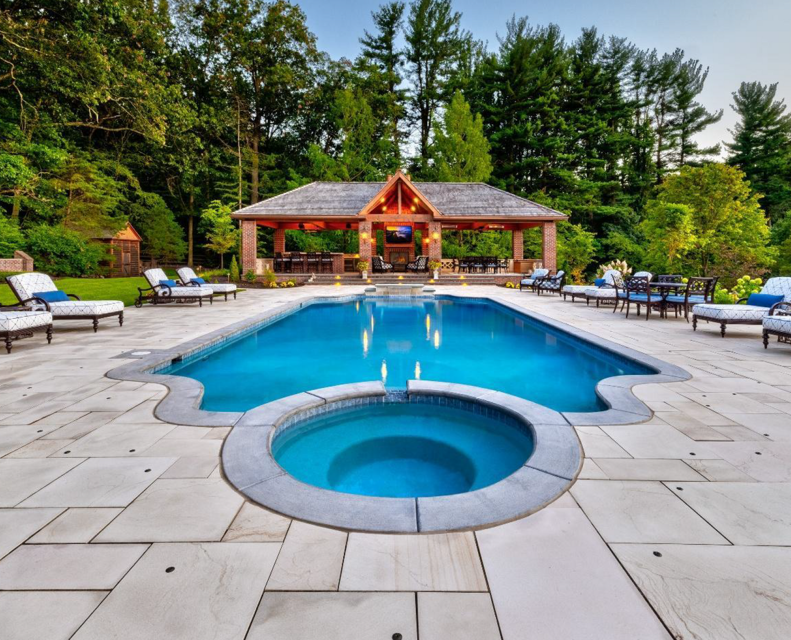 A large swimming pool is lit up at night in front of a house.