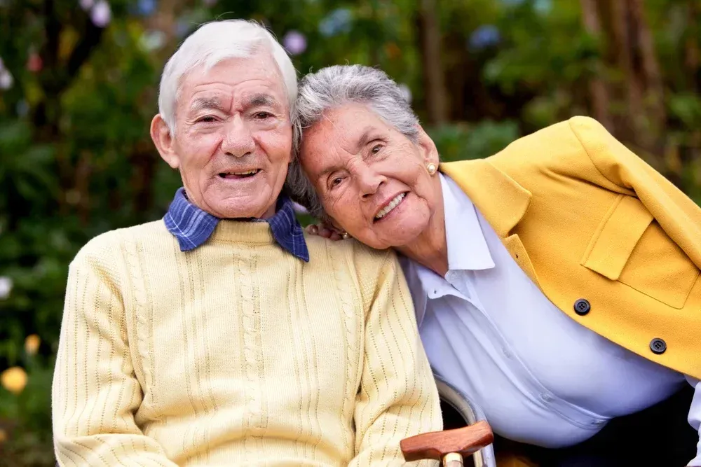An elderly man and woman are posing for a picture . the woman is wearing a yellow jacket.