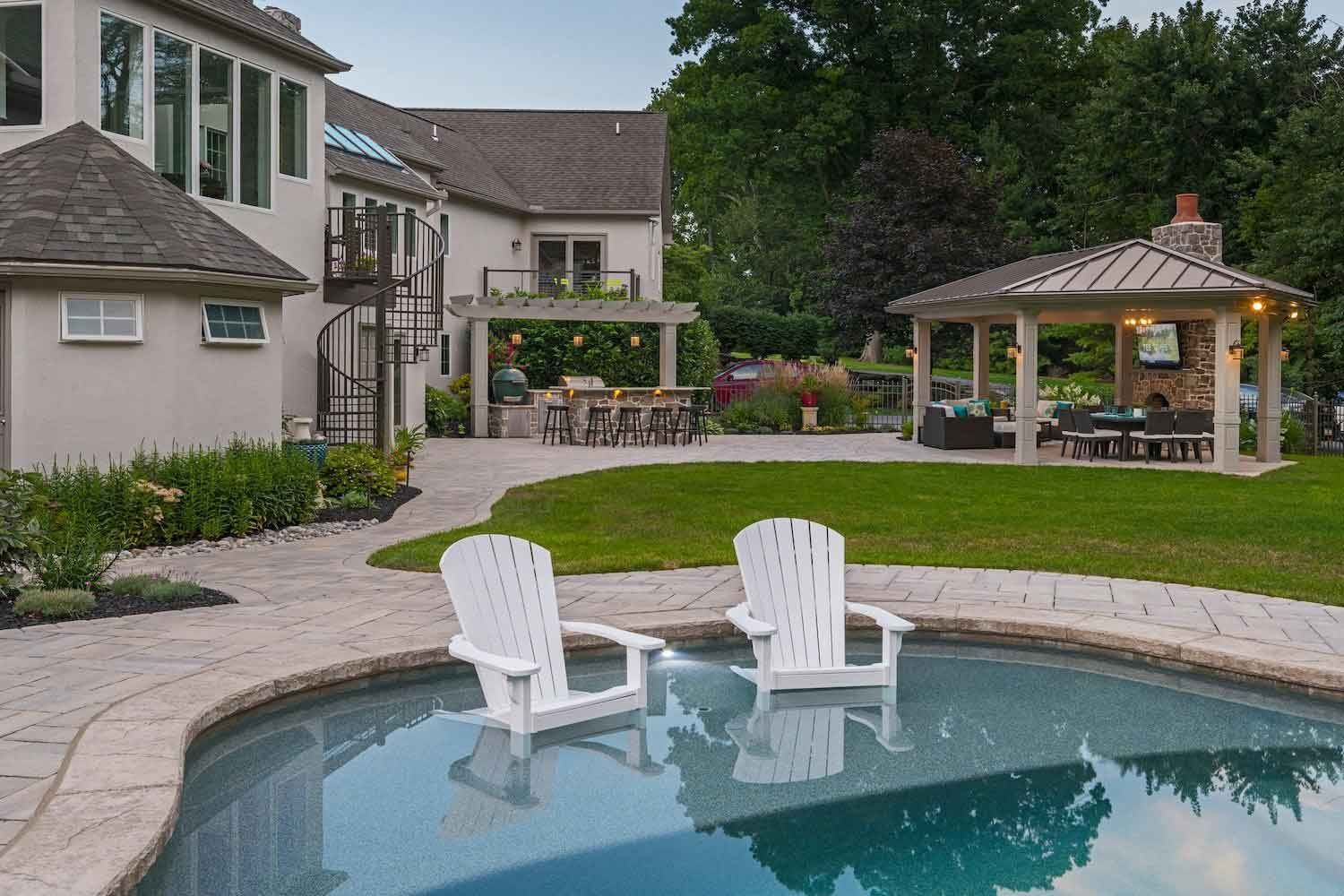 Two white chairs are sitting next to a swimming pool in a backyard.