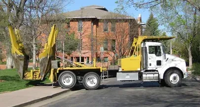 A yellow and white dump truck is parked on the side of the road in front of a brick building.