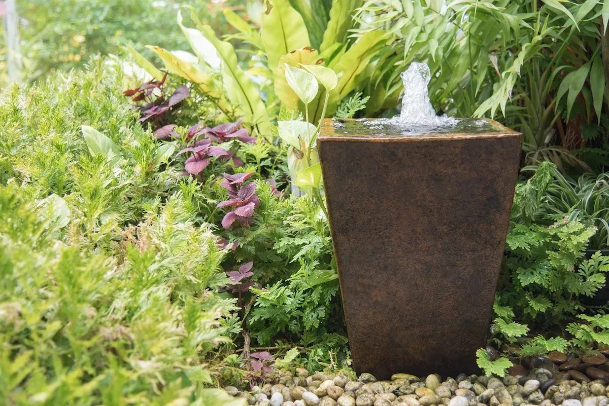 A water fountain in a garden surrounded by plants and rocks.