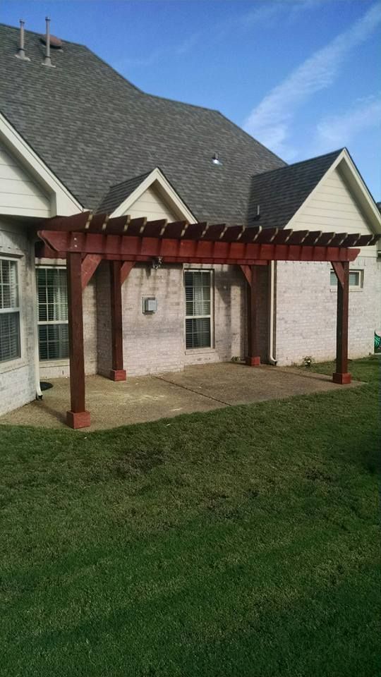 Red pergola attached to a brick house over a concrete patio and lawn.