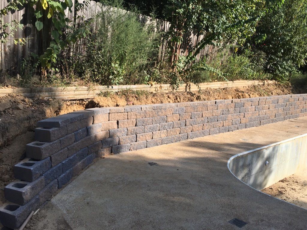 Retaining wall made of dark brown bricks and light brown ground, built in a yard.
