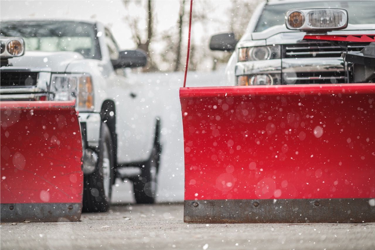 Two snow plows are parked next to each other in a parking lot.