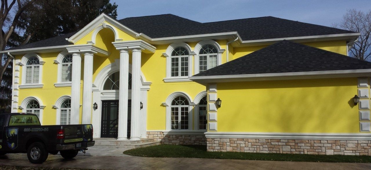 Large yellow mansion with white trim and arched entryway, seen from the front with a parked vehicle.