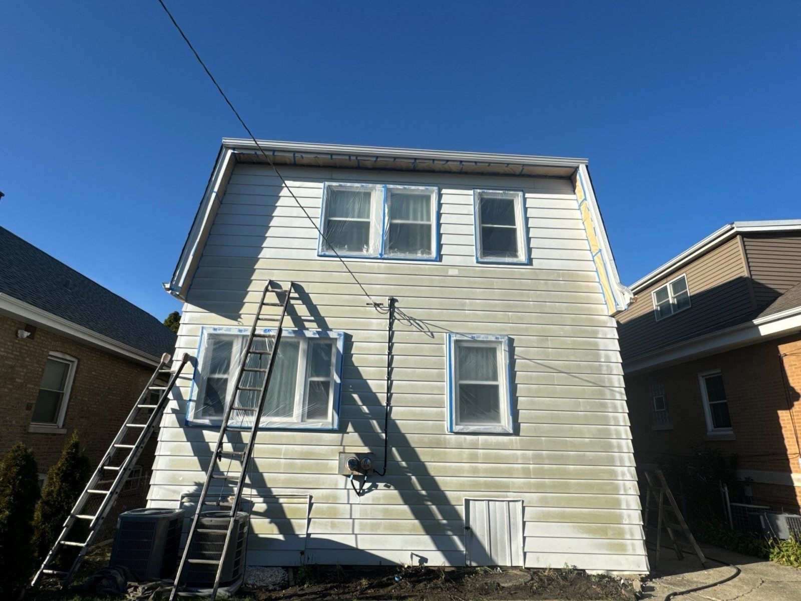 Back of a white two-story house with exterior metal stairs and neighboring homes under a blue sky