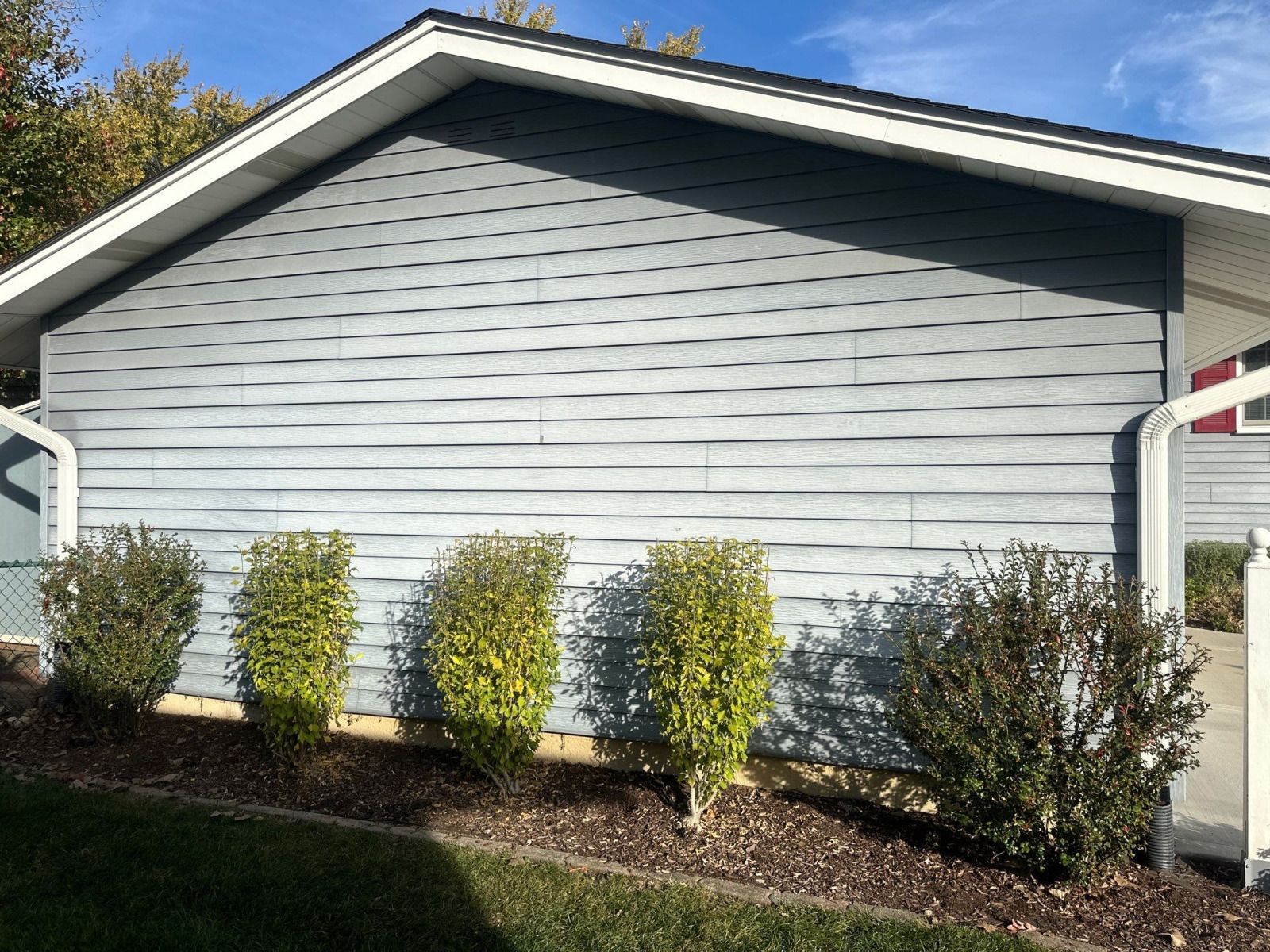 Gray house siding with a gable roof and trimmed shrubs in front