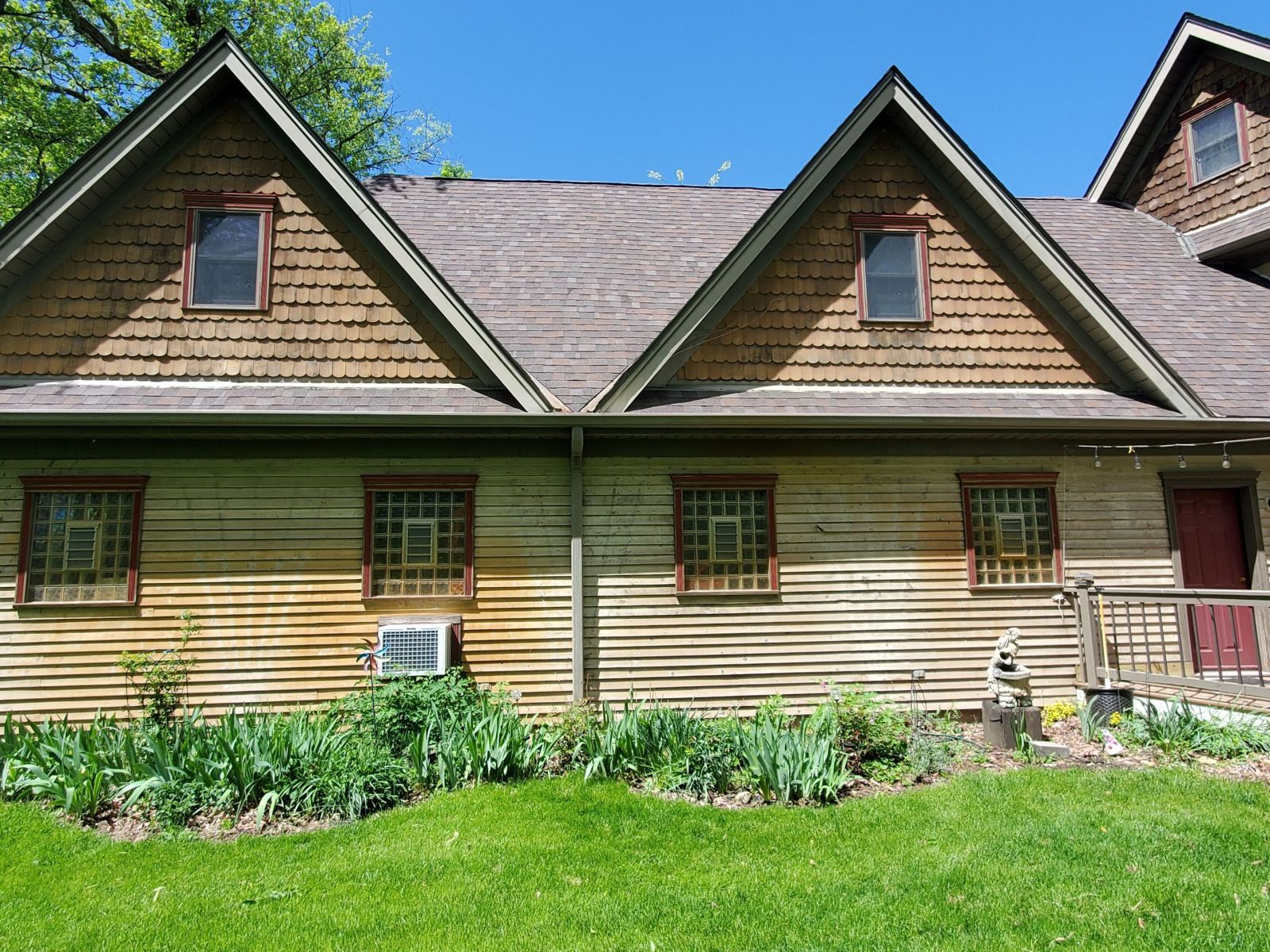 A rustic lodge with three peaked dormers, tan siding, green trim, and a grassy front lawn.