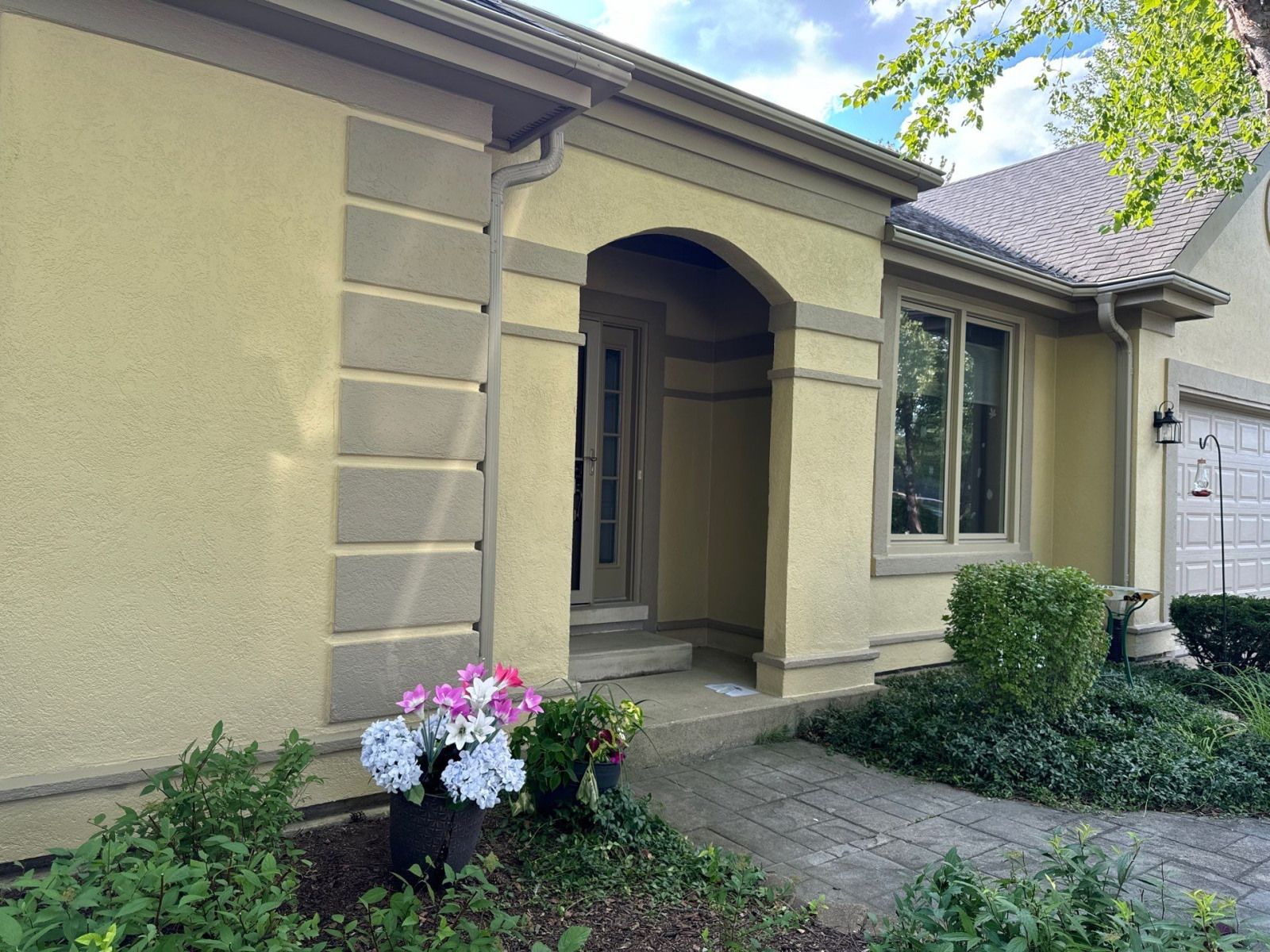 Front entrance of a beige stucco house with an arched porch, stone path, and flower planter by the door