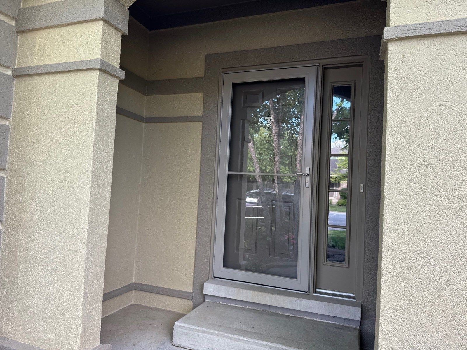 Front entry with a gray door, glass storm door, and beige stucco walls