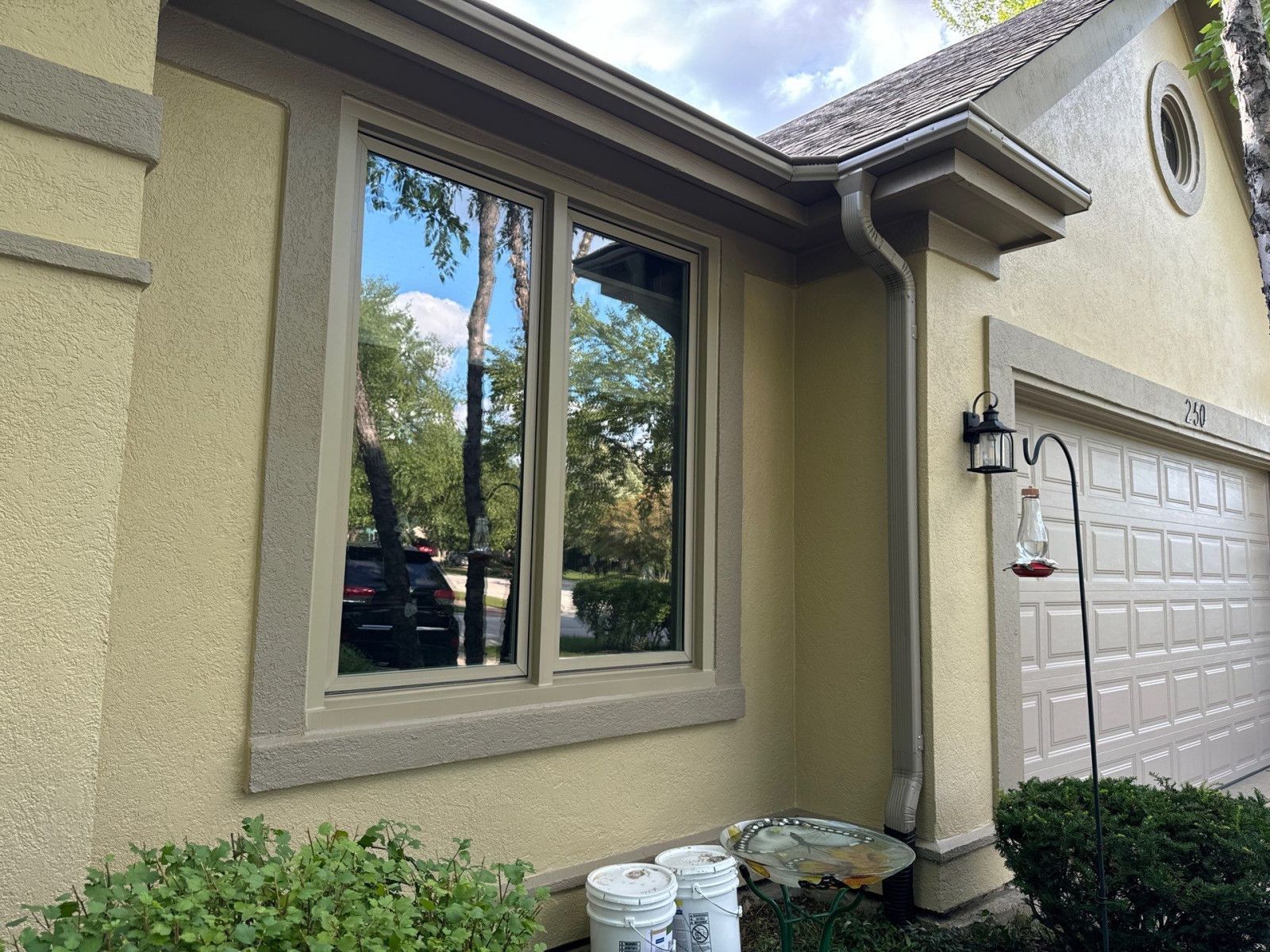 House exterior with beige stucco wall, window, garage door, and stacked buckets near the entry column
