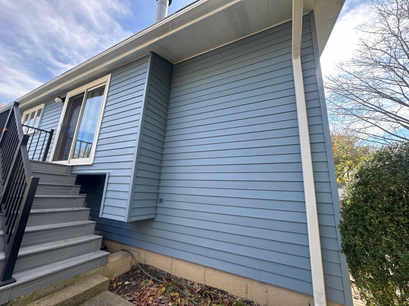 Light blue house exterior with stairs, windows, and a side wall beside bushes