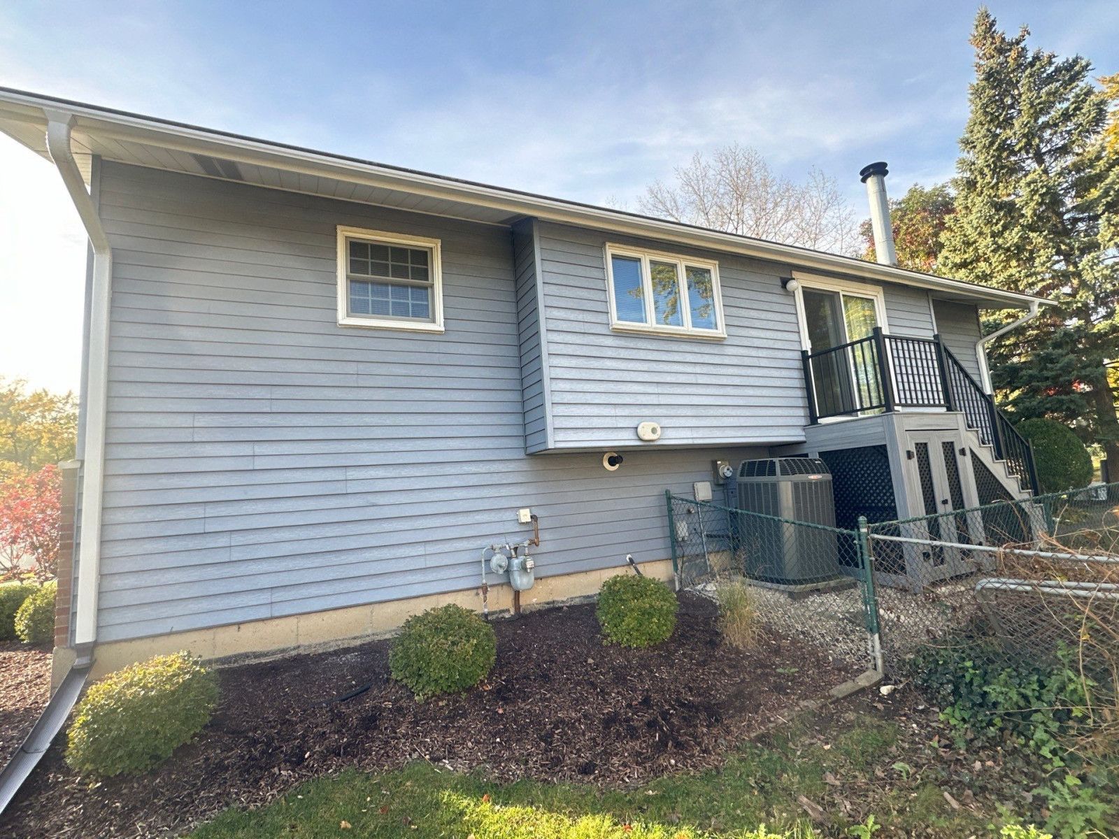Blue two-story house exterior with white trim, small front garden, and stairs to a side entrance