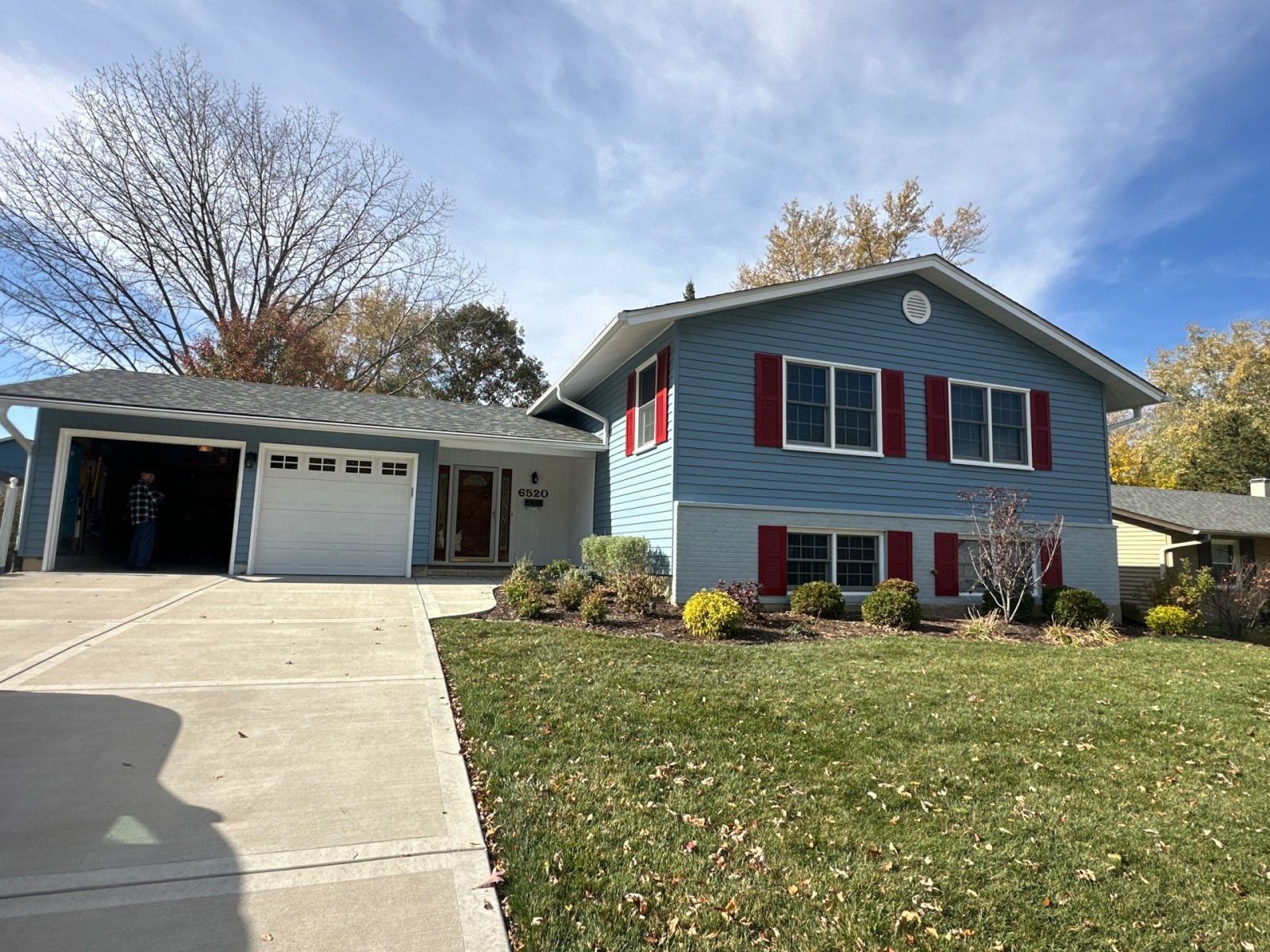 Suburban house with light blue siding, red shutters, attached garage, and a concrete driveway.