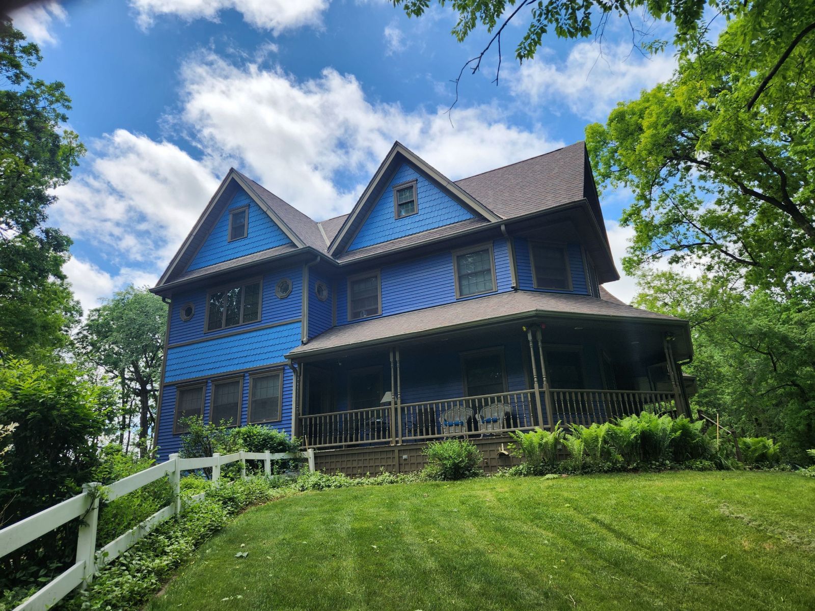Blue Victorian-style house on a grassy hill under a bright, partly cloudy sky