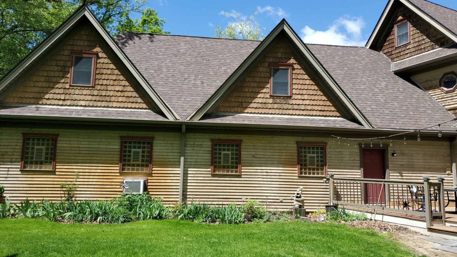 Rustic wooden cottage with green grass, dormer windows, and a red door under a blue sky