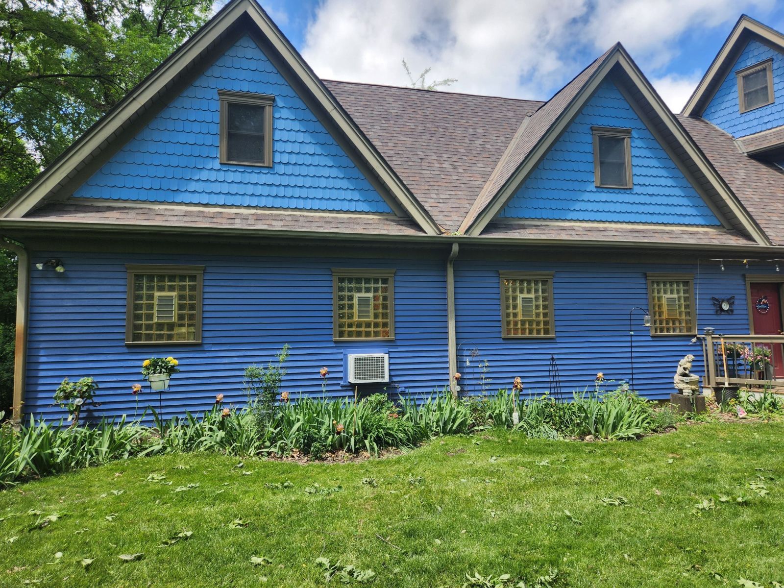 Blue house with two gabled dormers, a garden bed, and a green lawn.