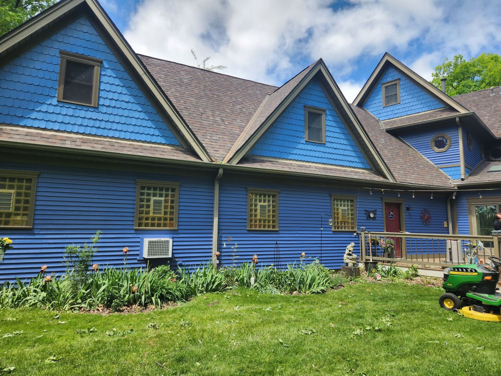 Blue house with steep gabled roof, screened porch, and green lawn under a partly cloudy sky