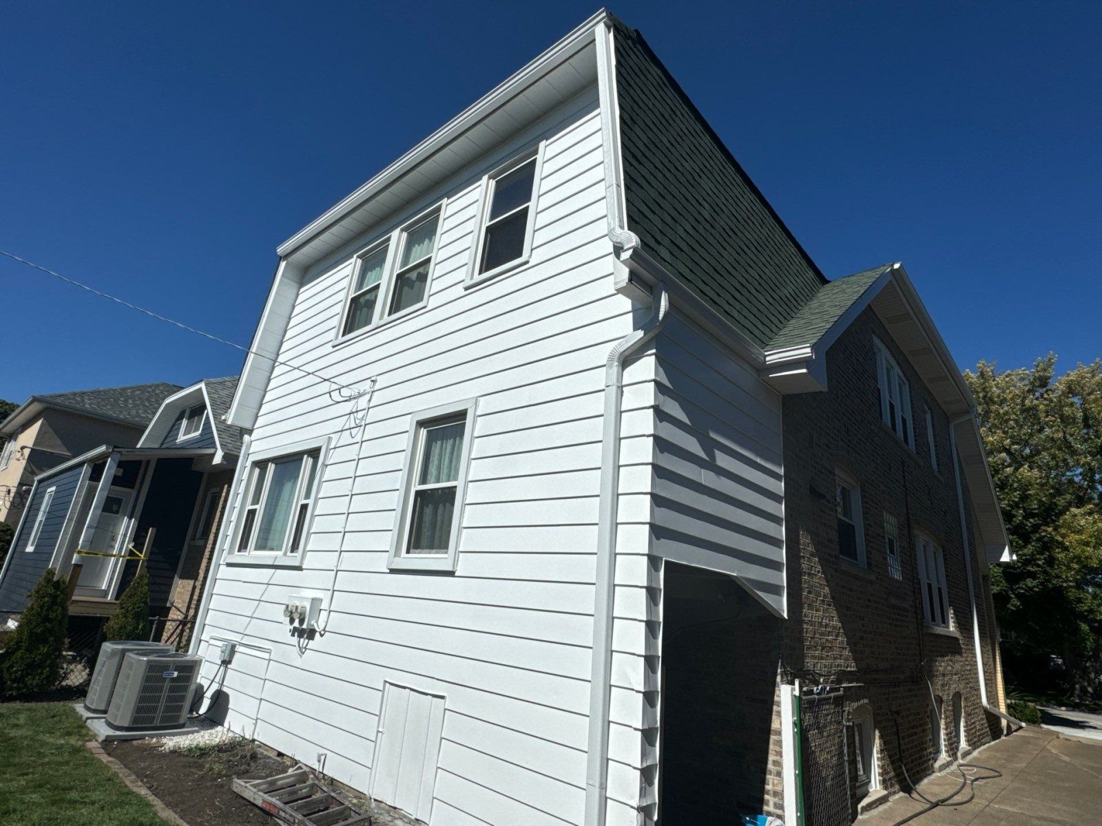 White two-story house with gray trim and brick side wall under a clear blue sky