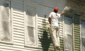 Worker painting the exterior wall of a house while standing on a ladder
