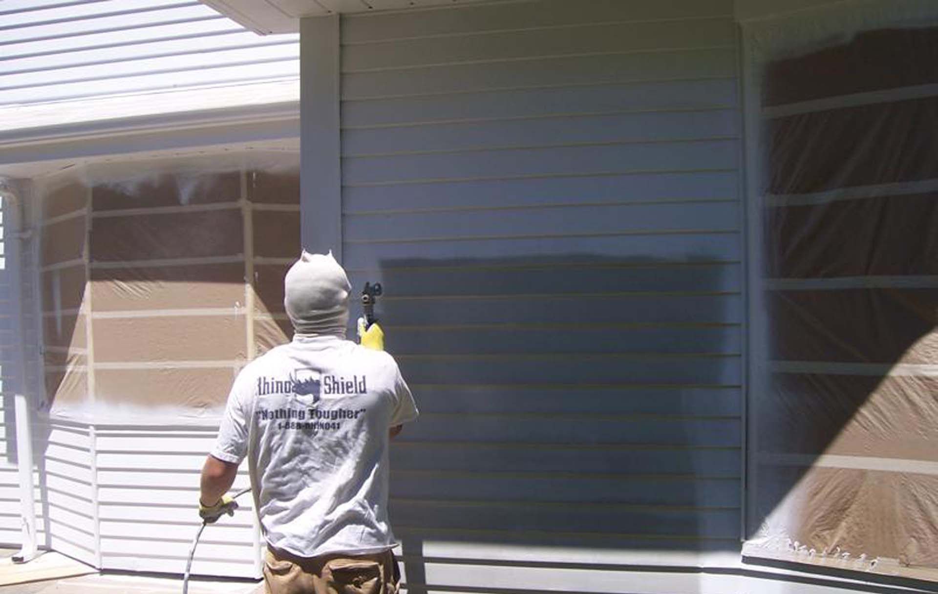 Person painting a house exterior wall beside a window, with part of the wall covered in plastic.