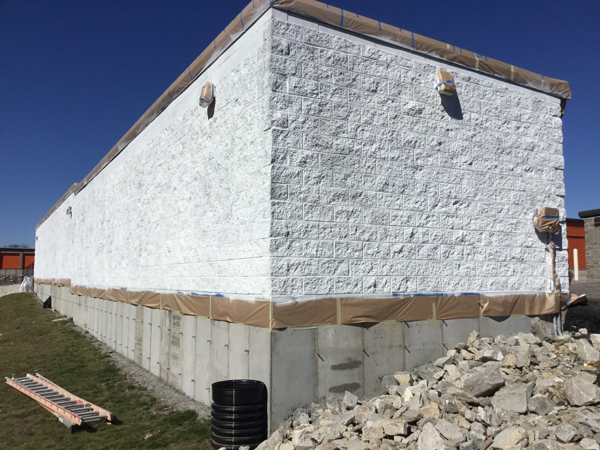White stone-sided building under construction with exposed foundation and rubble beside it