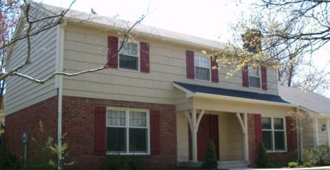 Two-story beige and red brick suburban house with maroon shutters and a front porch