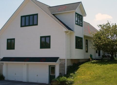 White two-story house with dark-trimmed windows, a garage, and a grassy hillside in front