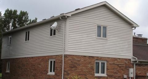 Two-story house with white siding and red brick lower level, seen from the side under an overcast sky