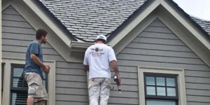 Two workers on a roof inspecting gray siding and shingles on a house