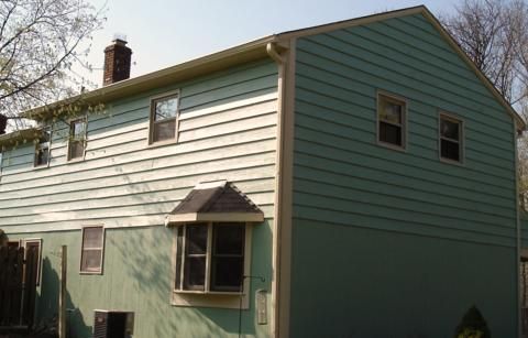 Two-story green house with white siding and small windows in daylight