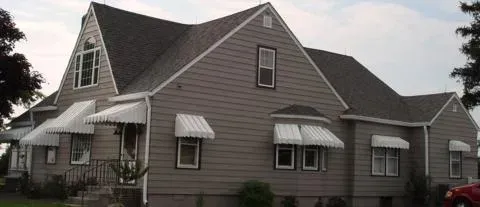 Gray house with multiple dormers and white awnings, viewed from the front yard