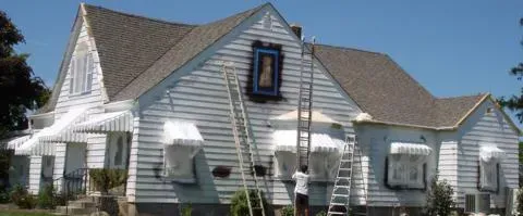 White house with gray roof and blue sky, featuring a steep gable and a small central dormer window.